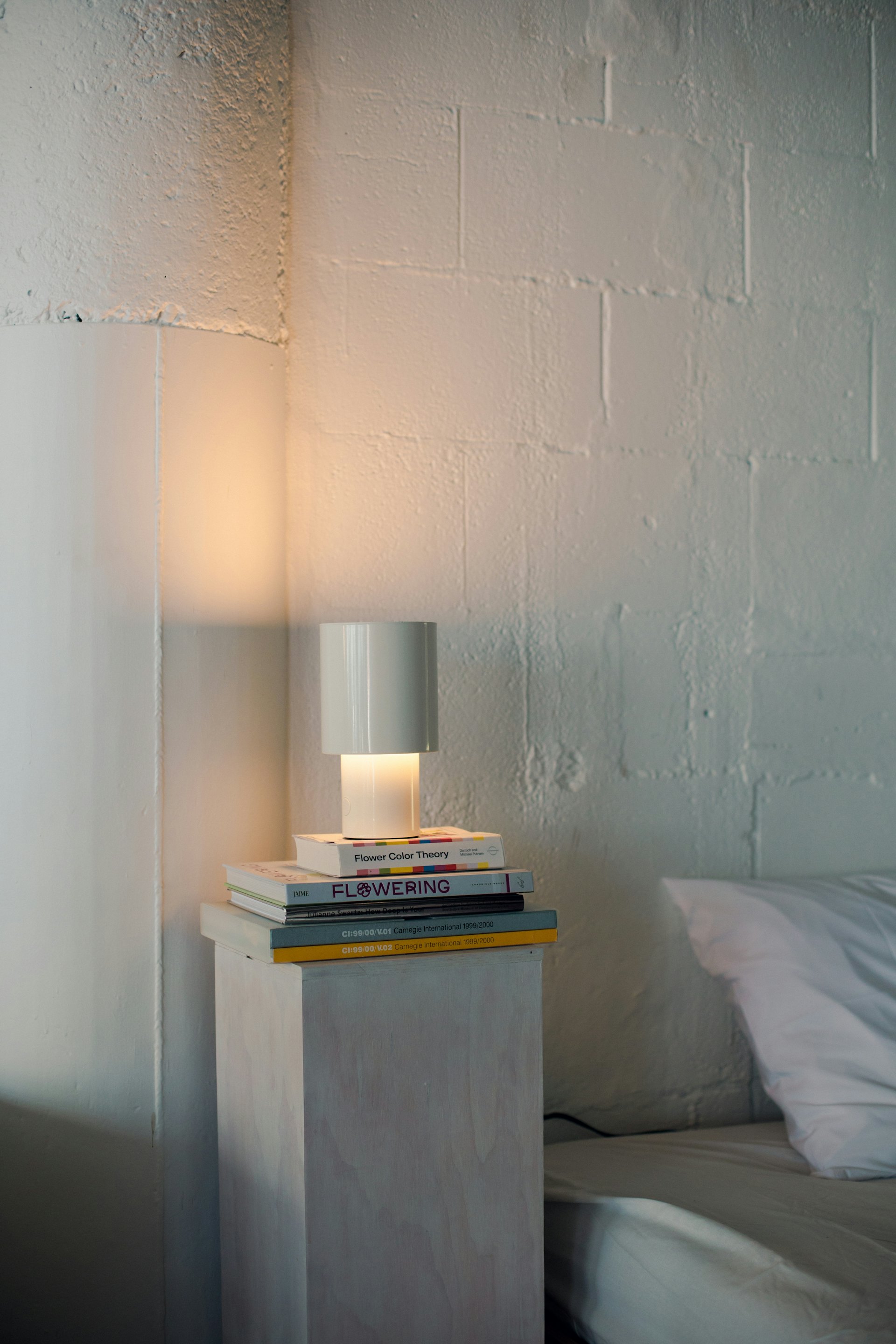 A small white lamp on a stack of books beside a bed